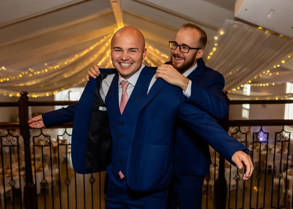 Groomsmen in navy suits share laughs and drinks during wedding celebration.