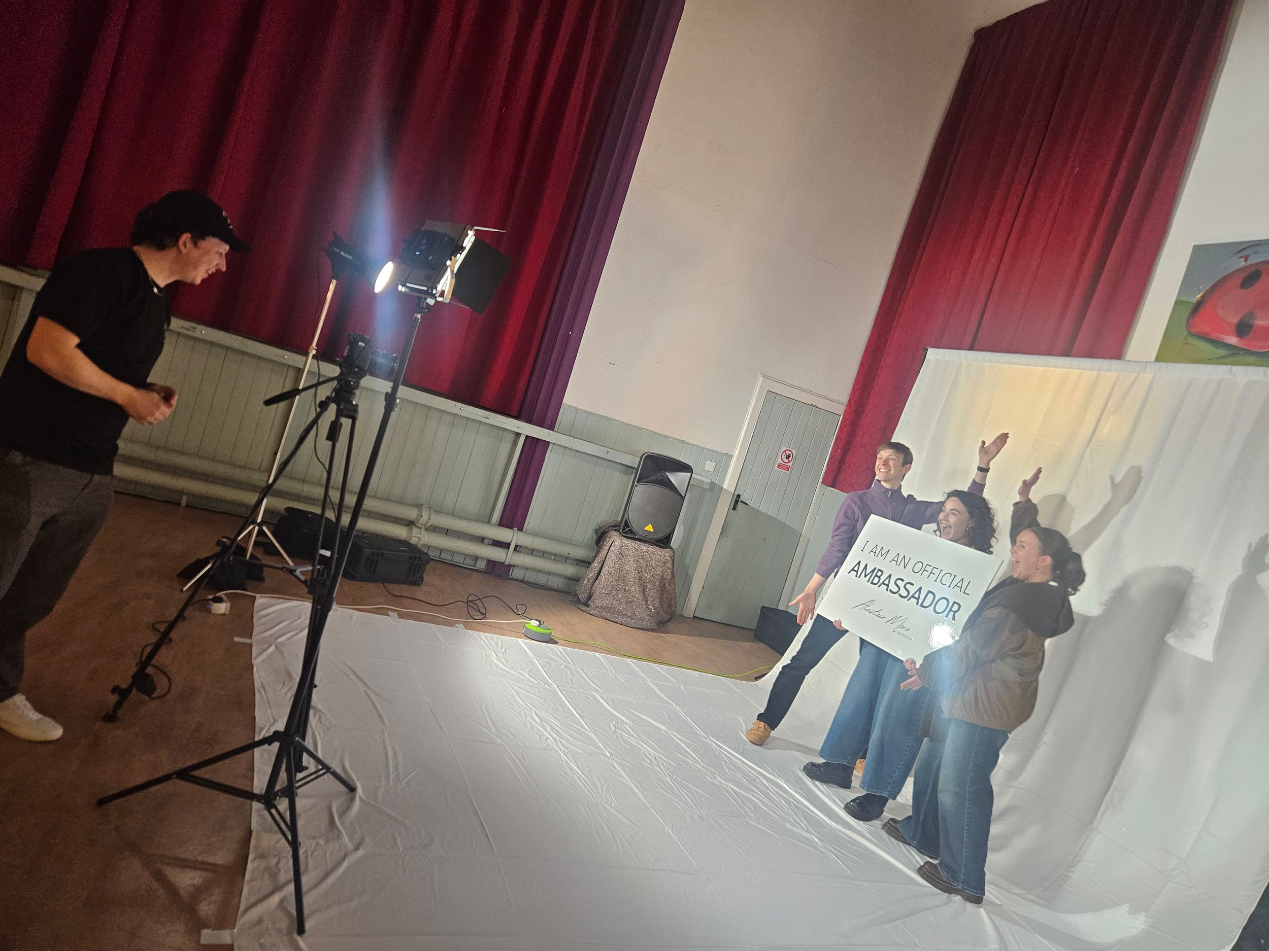 Behind the scenes setup of a photo or video shoot with lights, stands, and equipment in a studio space.