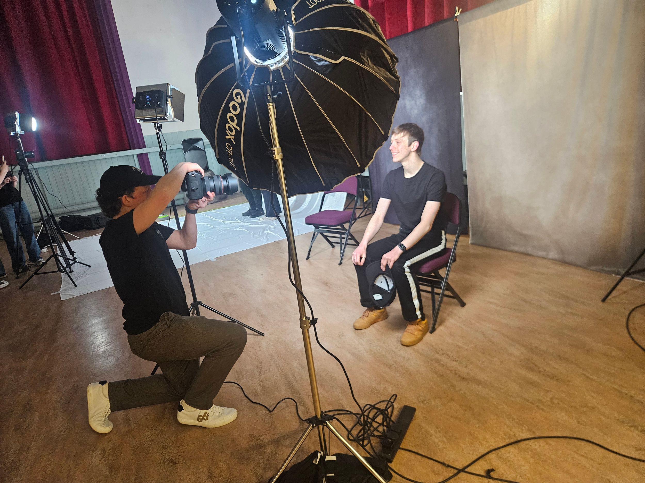 Behind the scenes photo shoot setup showing lighting equipment and camera gear in a studio with red curtains.