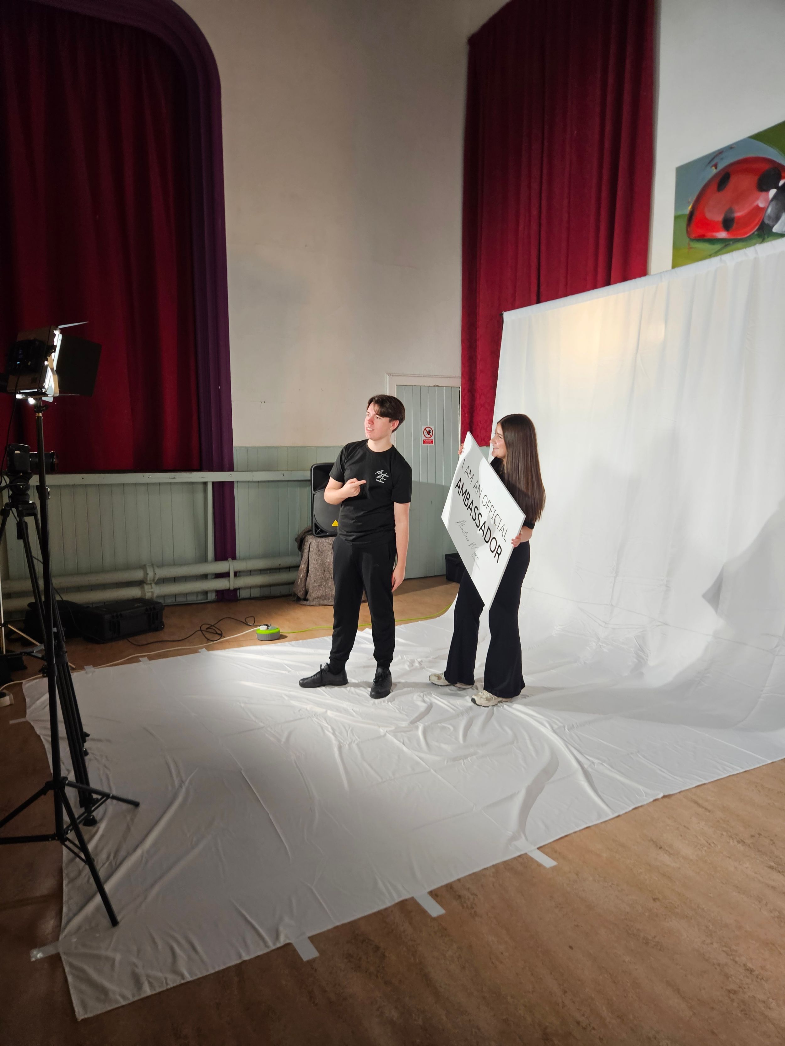 Behind-the-scenes photo shoot setup showing photographers working with white backdrop and red curtains in a studio space.