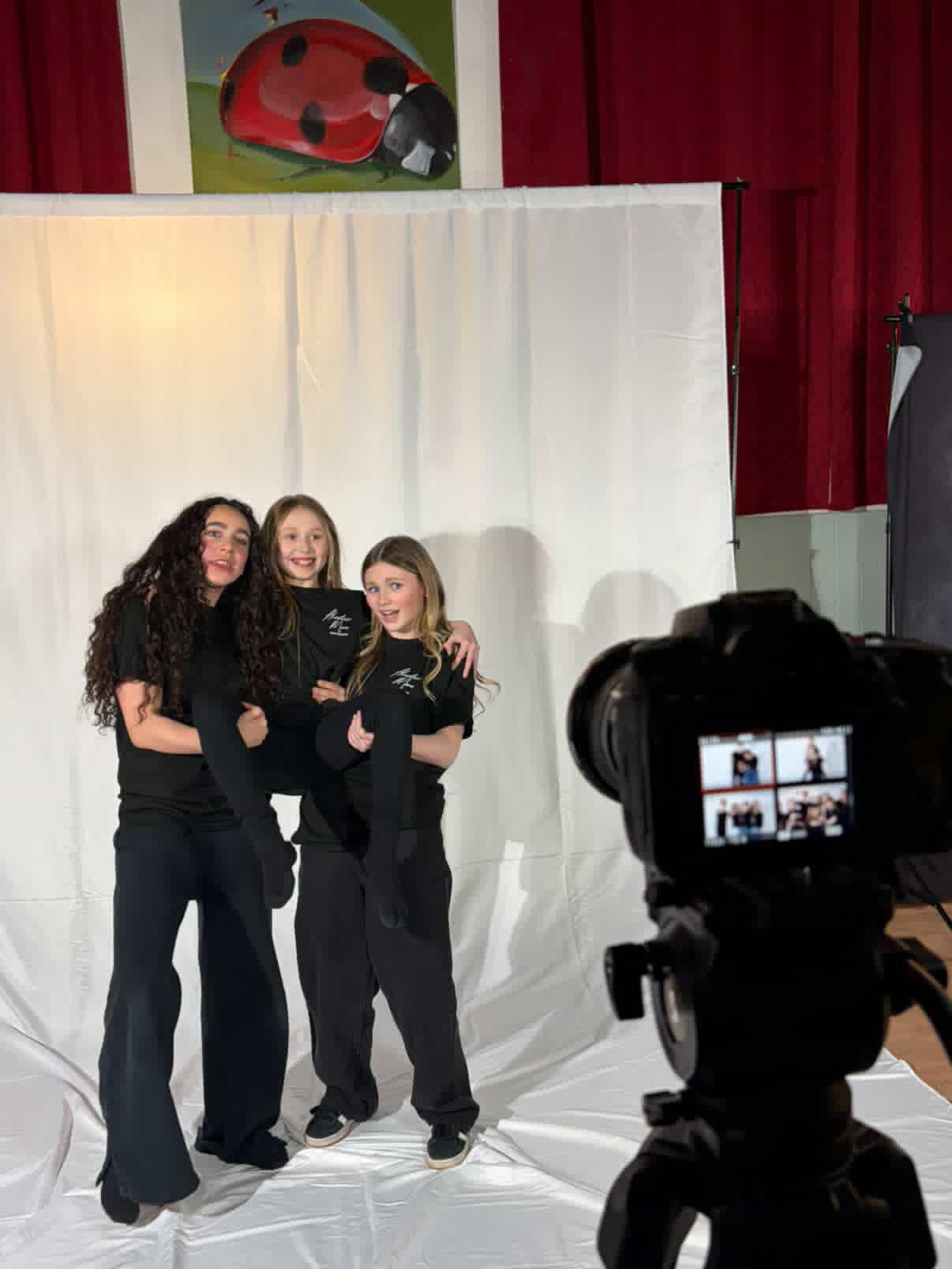 Three people in black outfits pose together against a white backdrop during a photo session.
