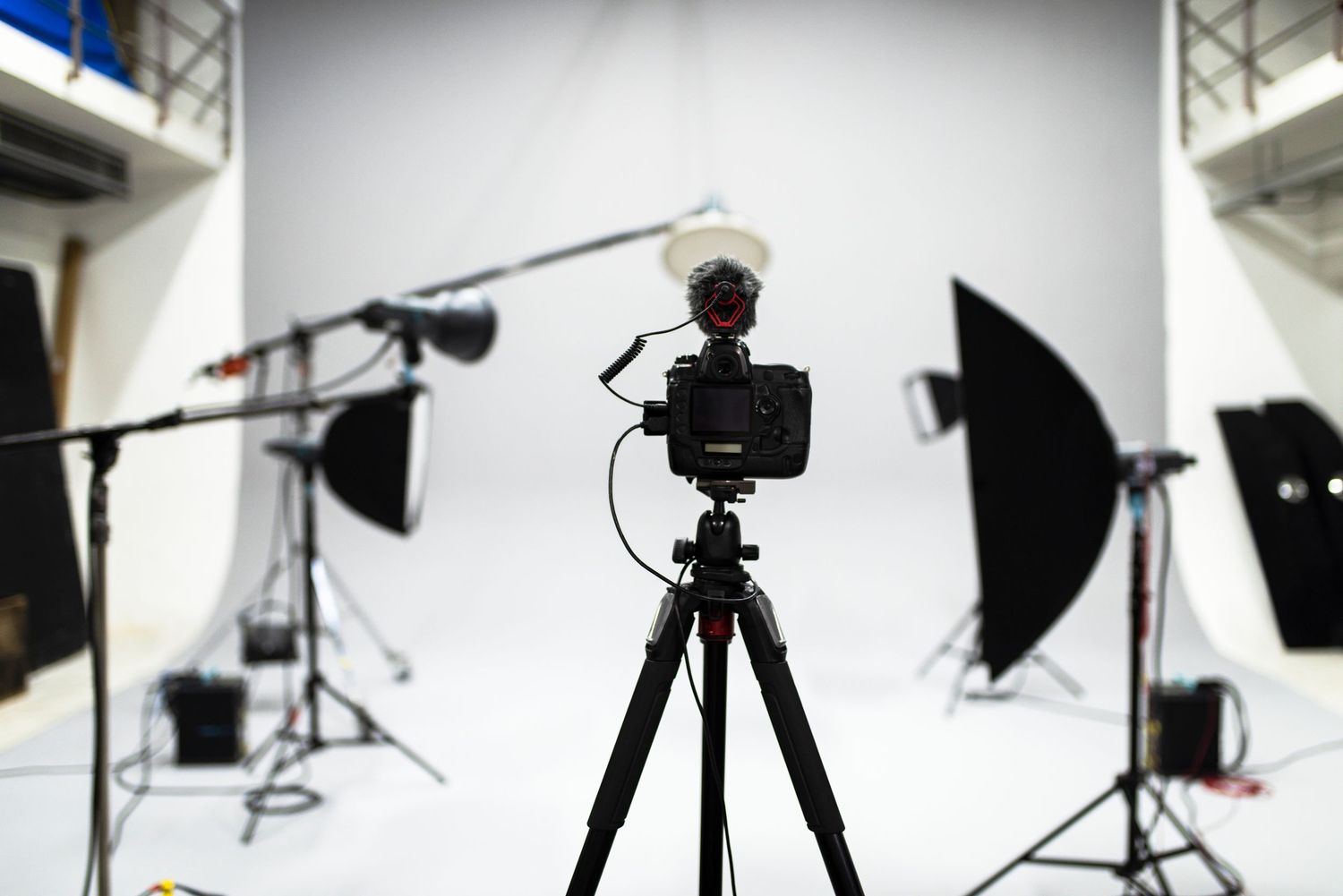 Professional photography studio setup with lighting equipment, reflectors, and camera gear silhouetted against white backdrop.