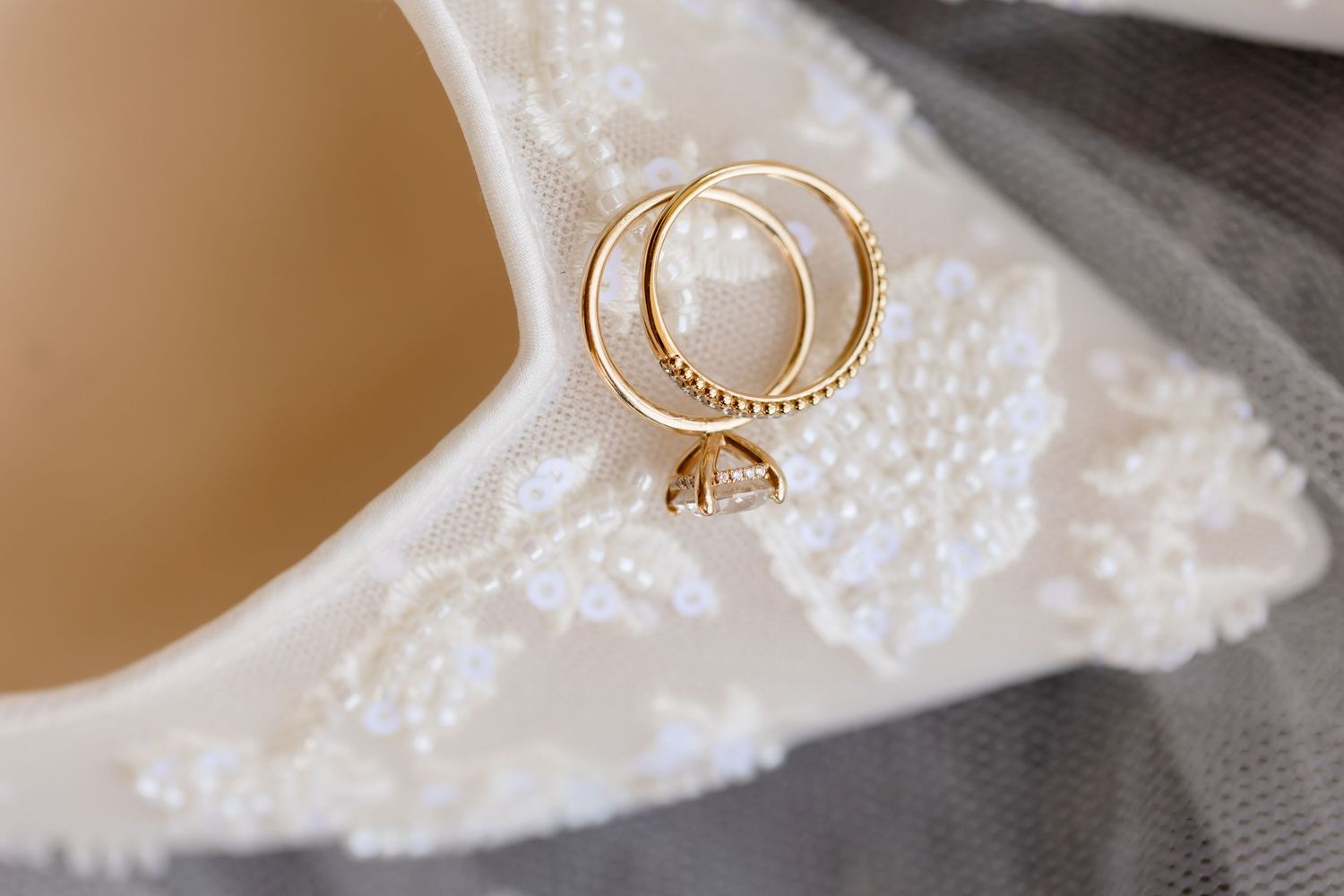 Gold wedding rings rest on delicate white lace fabric next to soft beige background.