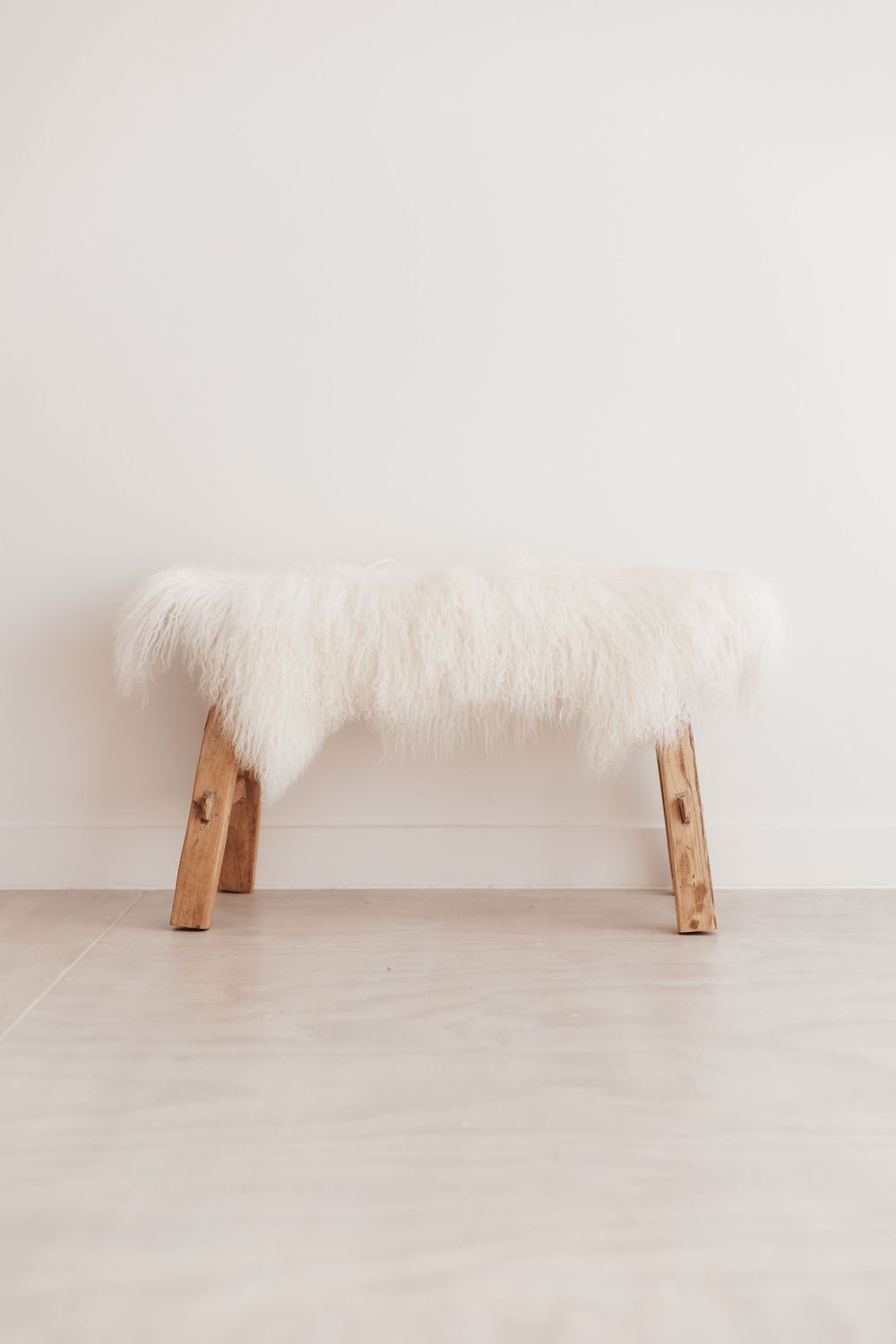 Simple wooden bench with white furry cushion against light wall.