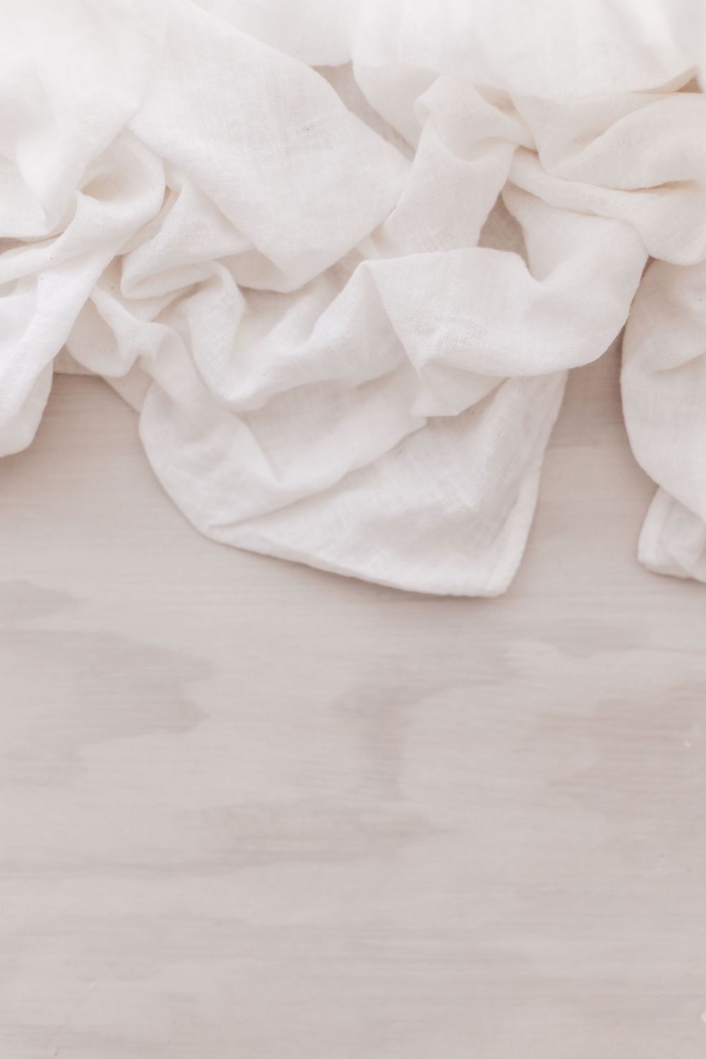 Soft white crumpled fabric texture on light surface creating gentle folds and shadows.