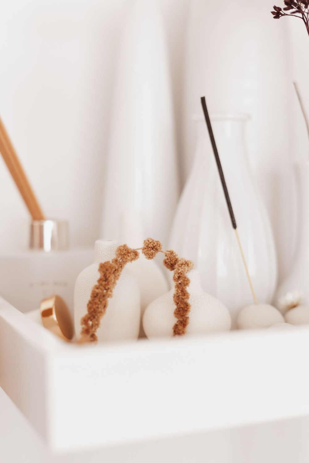 Decorative dried floral arch and white ceramic vessels on minimalist white tray.