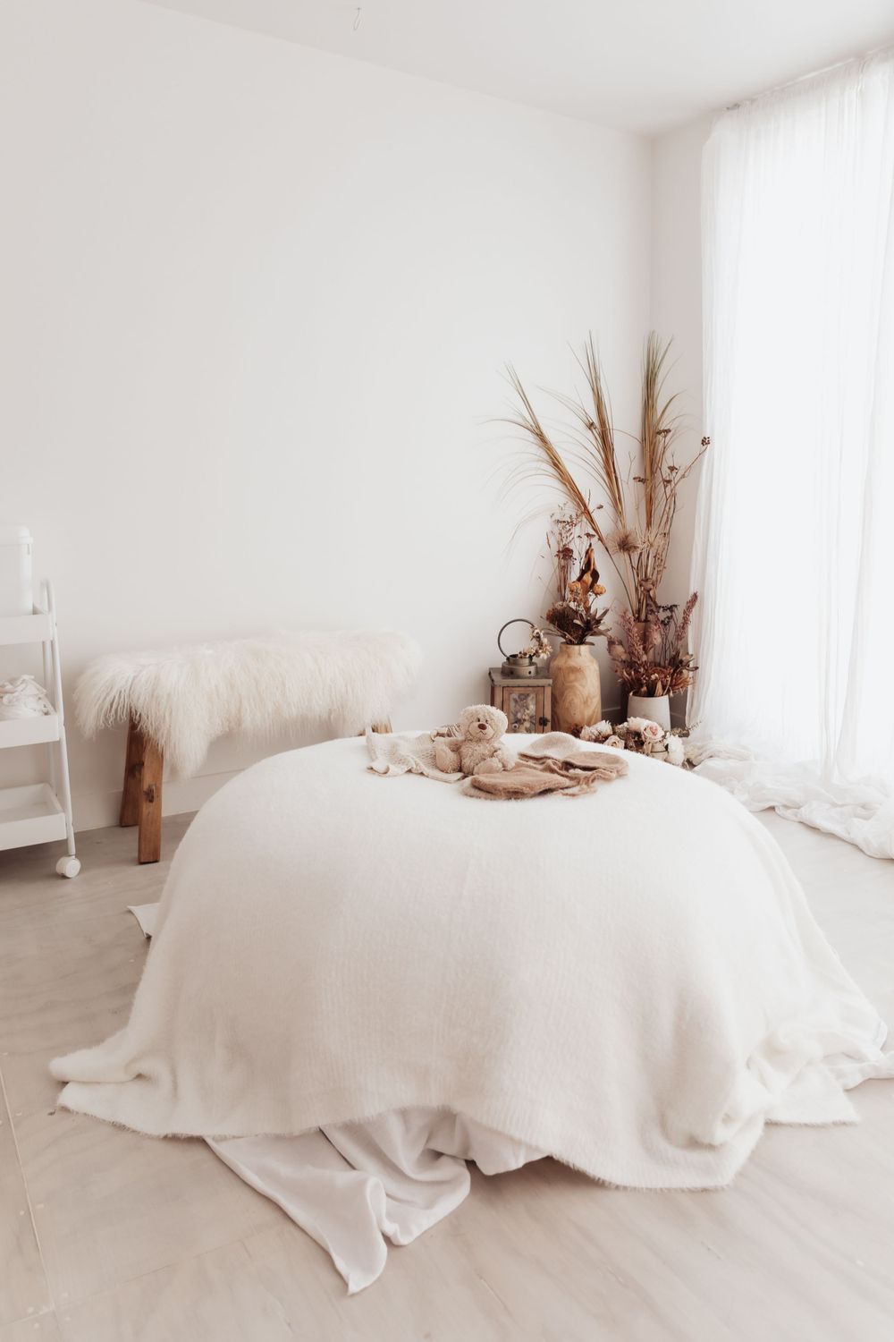 Minimalist bedroom with white bedding and dried floral arrangement on a round bed featuring neutral tones.