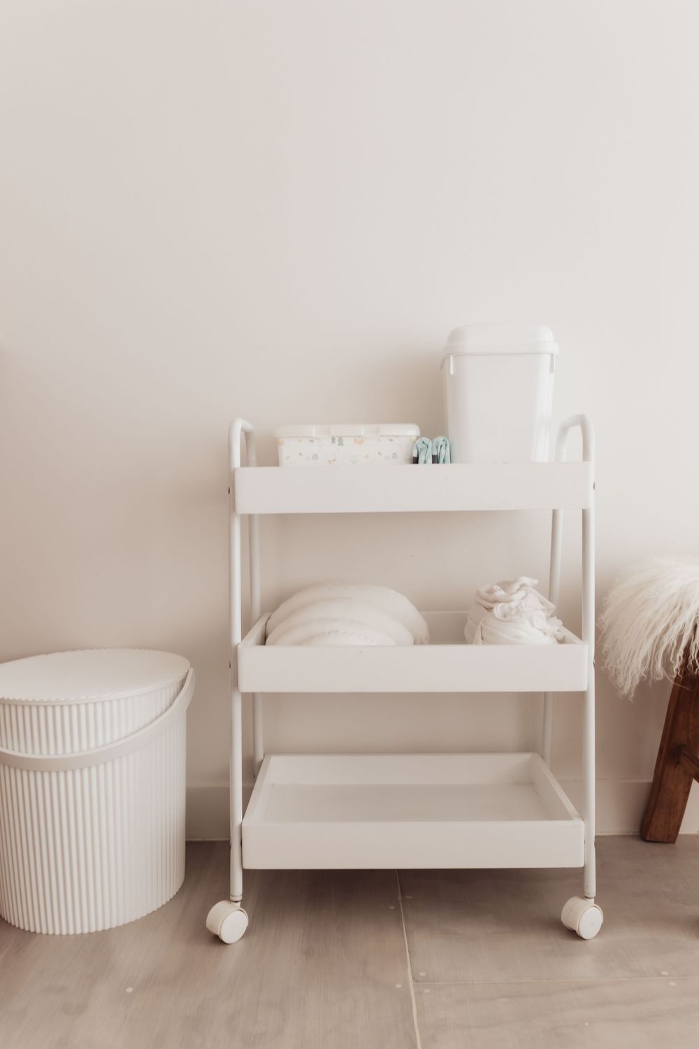 White rolling cart with storage shelves and a white cylindrical container beside it.