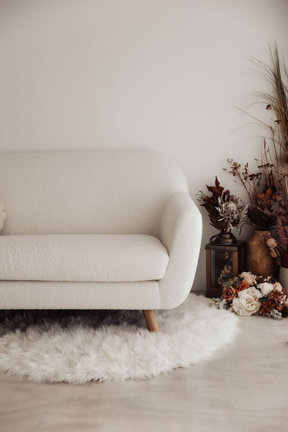 White sofa on plush faux fur rug with dried floral arrangements creating a cozy minimalist photography setup.