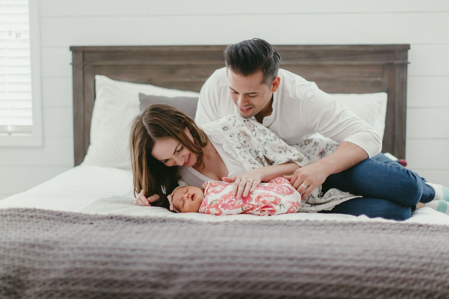 A sweet family moment on a gray bed with wooden headboard.