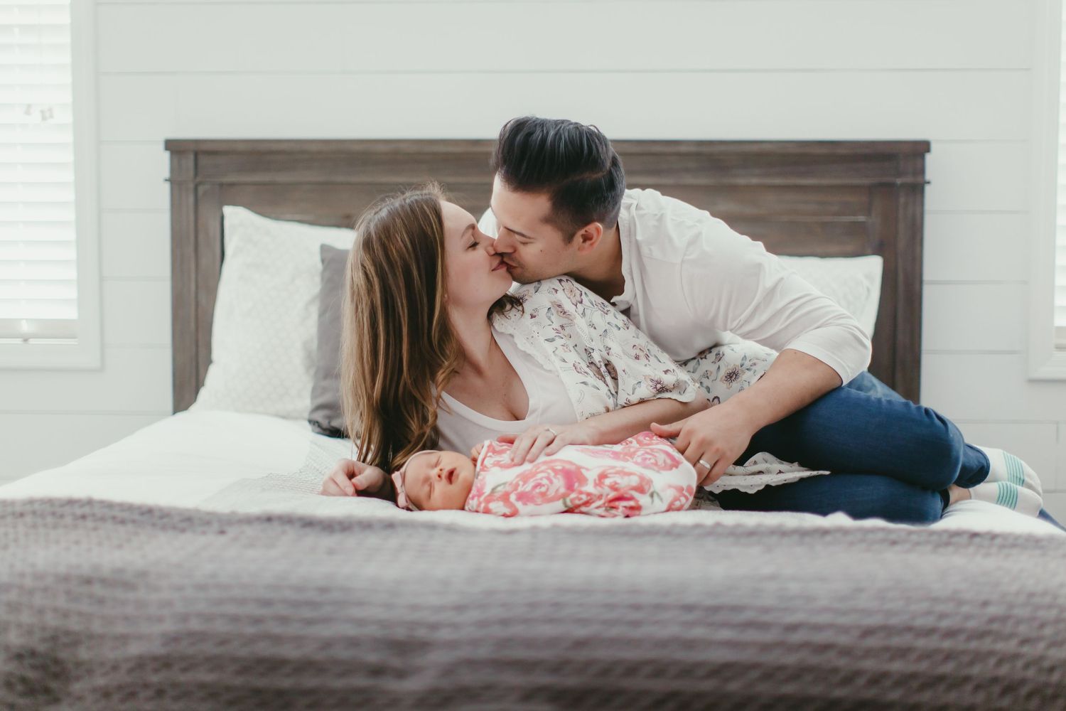 An intimate family portrait on a bed with a wooden headboard and white pillows.