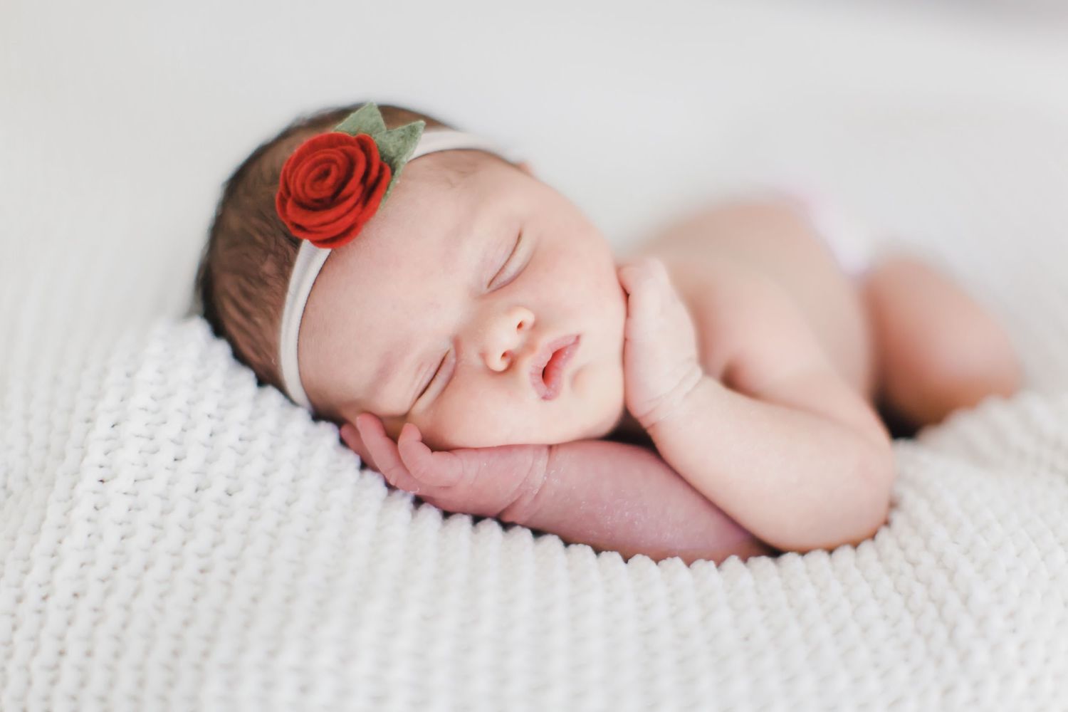 Newborn baby sleeping peacefully on soft white textured blanket.