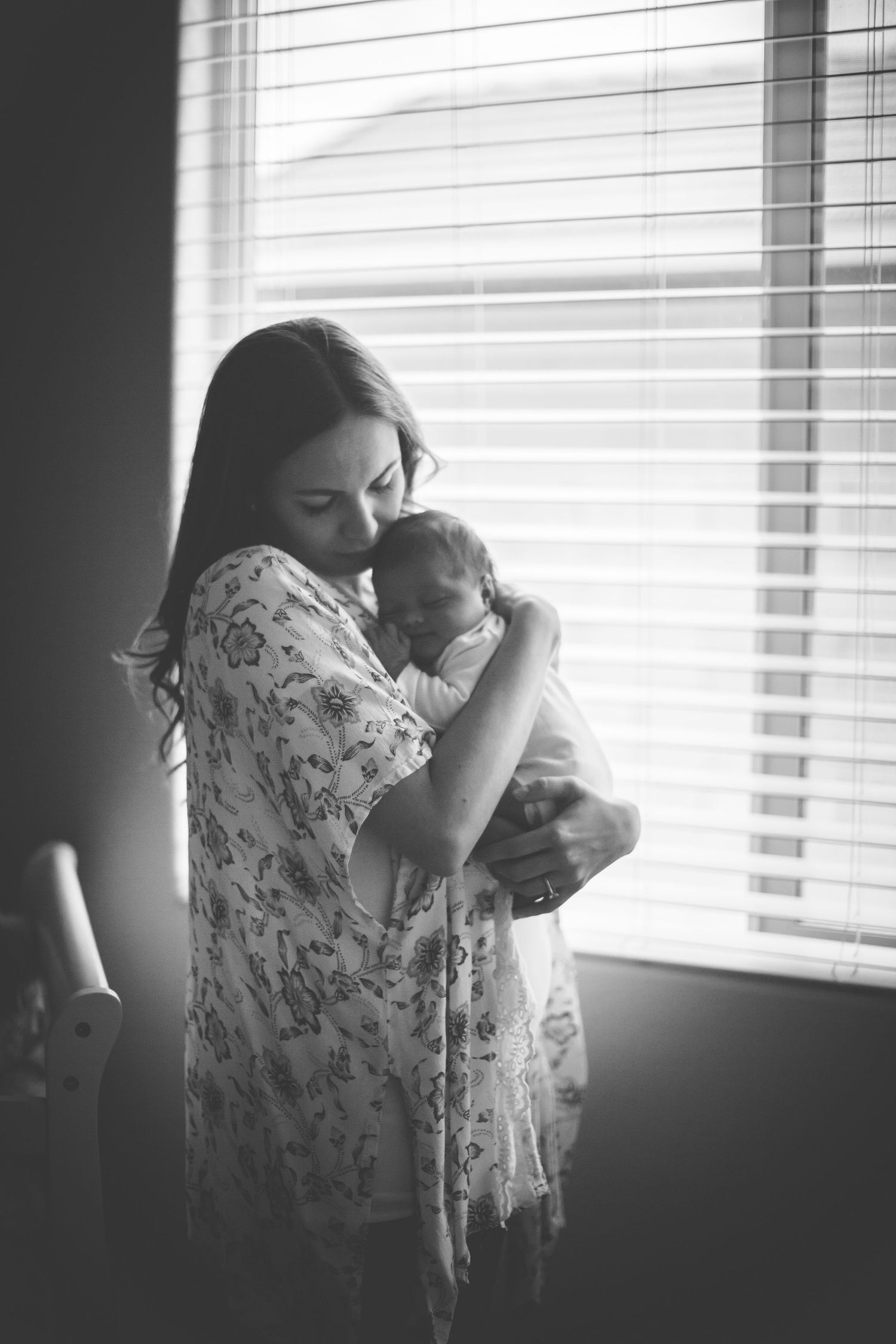 Intimate black and white family portrait series near window with natural lighting.