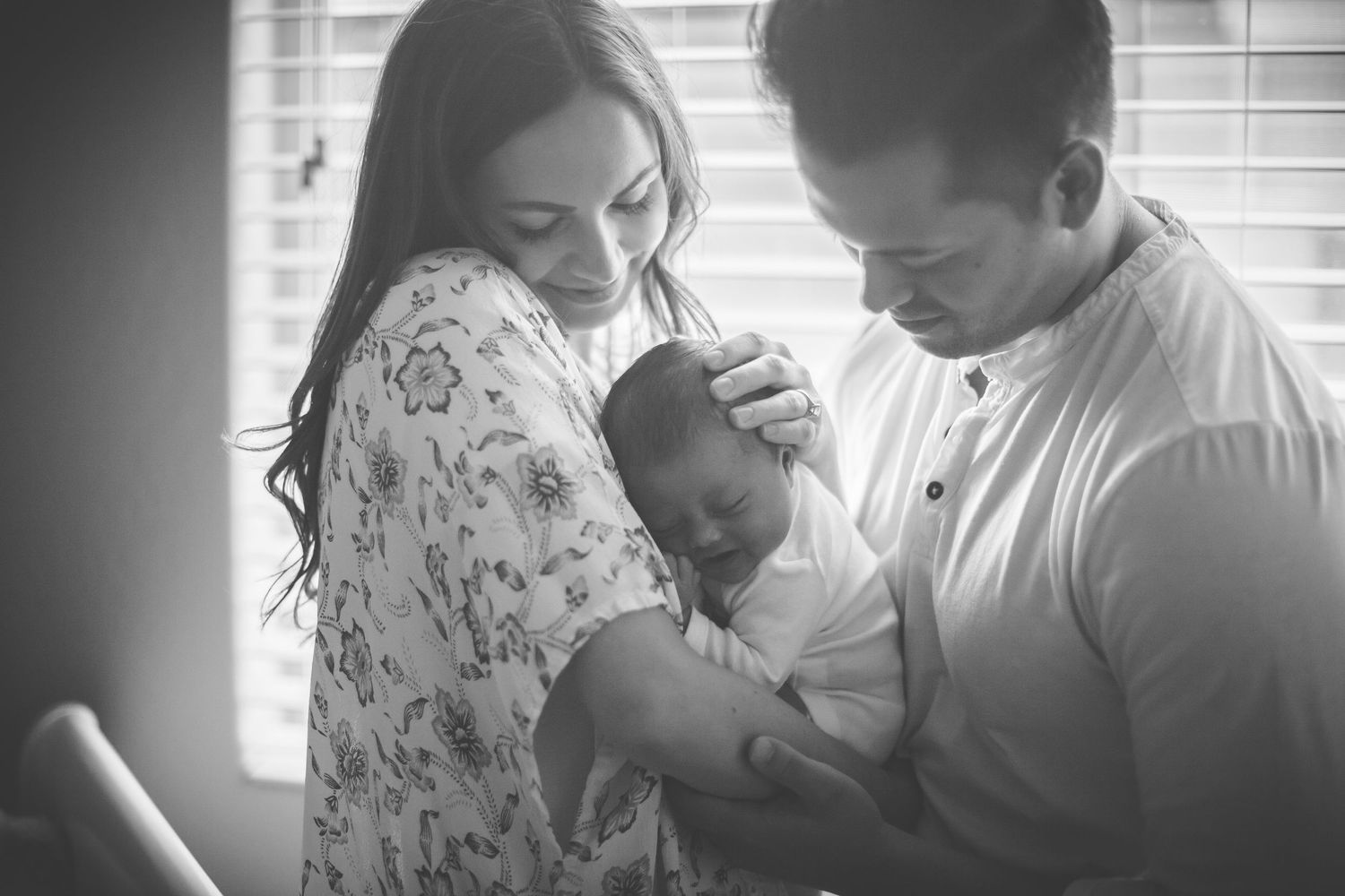 Emotional black and white family portrait series by window.