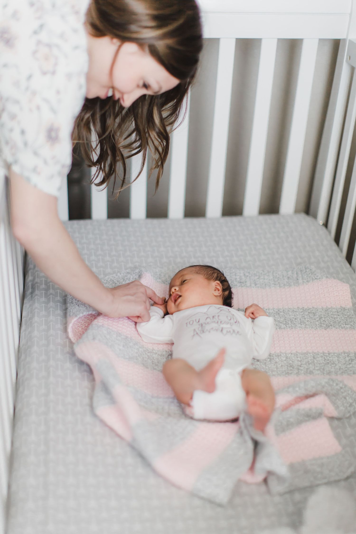 Baby resting in white crib with pink and grey bedding.