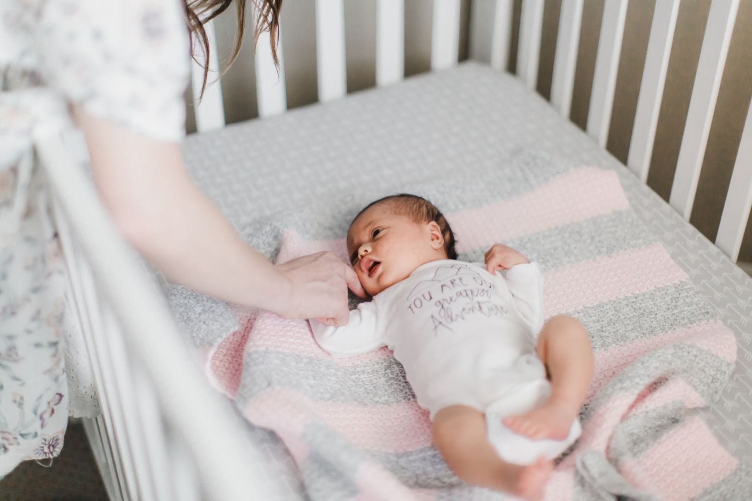 Newborn sleeping peacefully in white crib with pink accents.