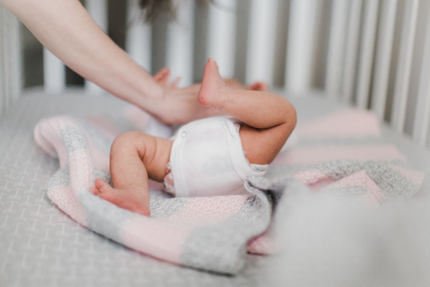 Gentle hands caring for newborn in white crib.