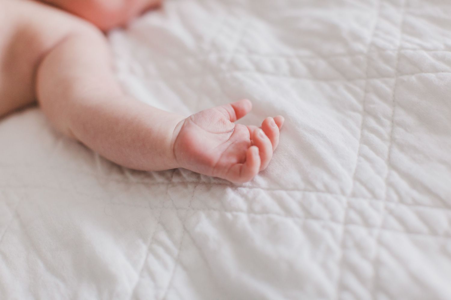 Close-up view of tiny newborn baby feet on white bedding.