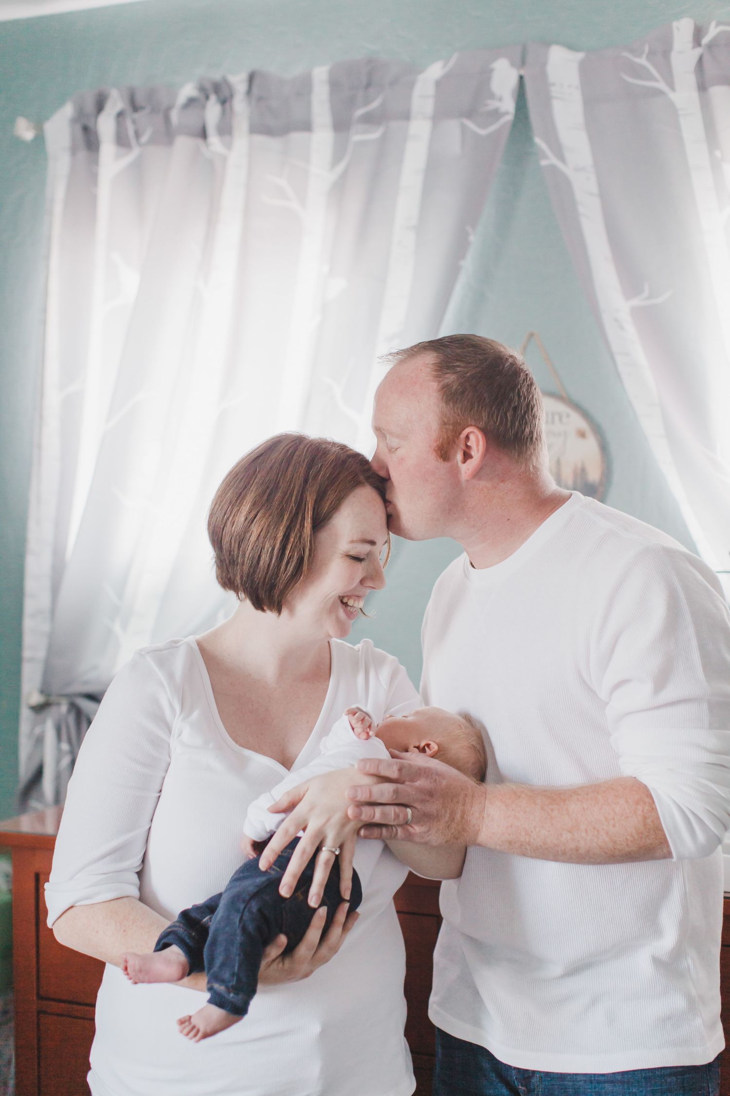 Family in white shirts sharing tender moments together against sheer curtains.