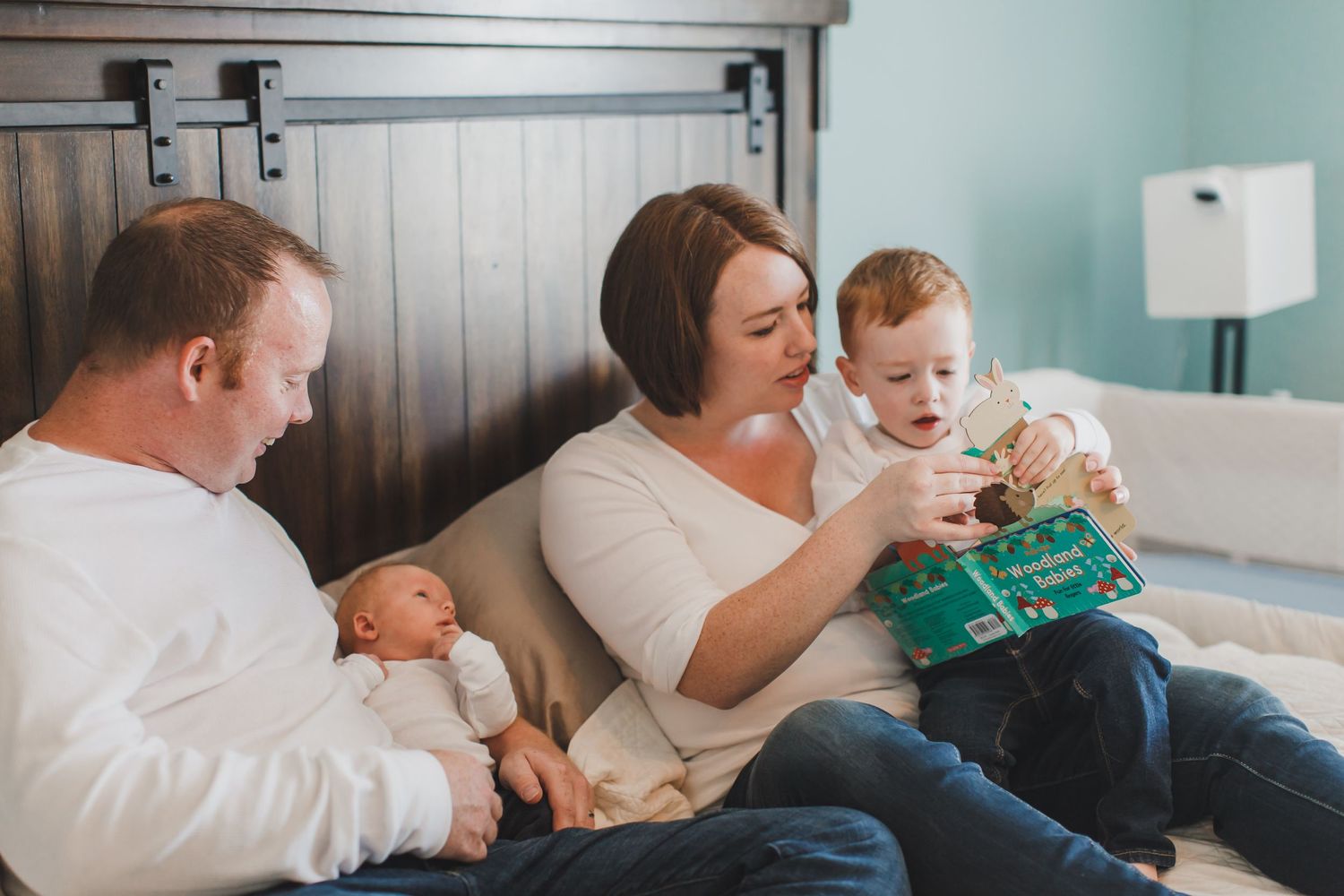 Family shares tender moments while sitting together on a couch in a bright nursery setting.