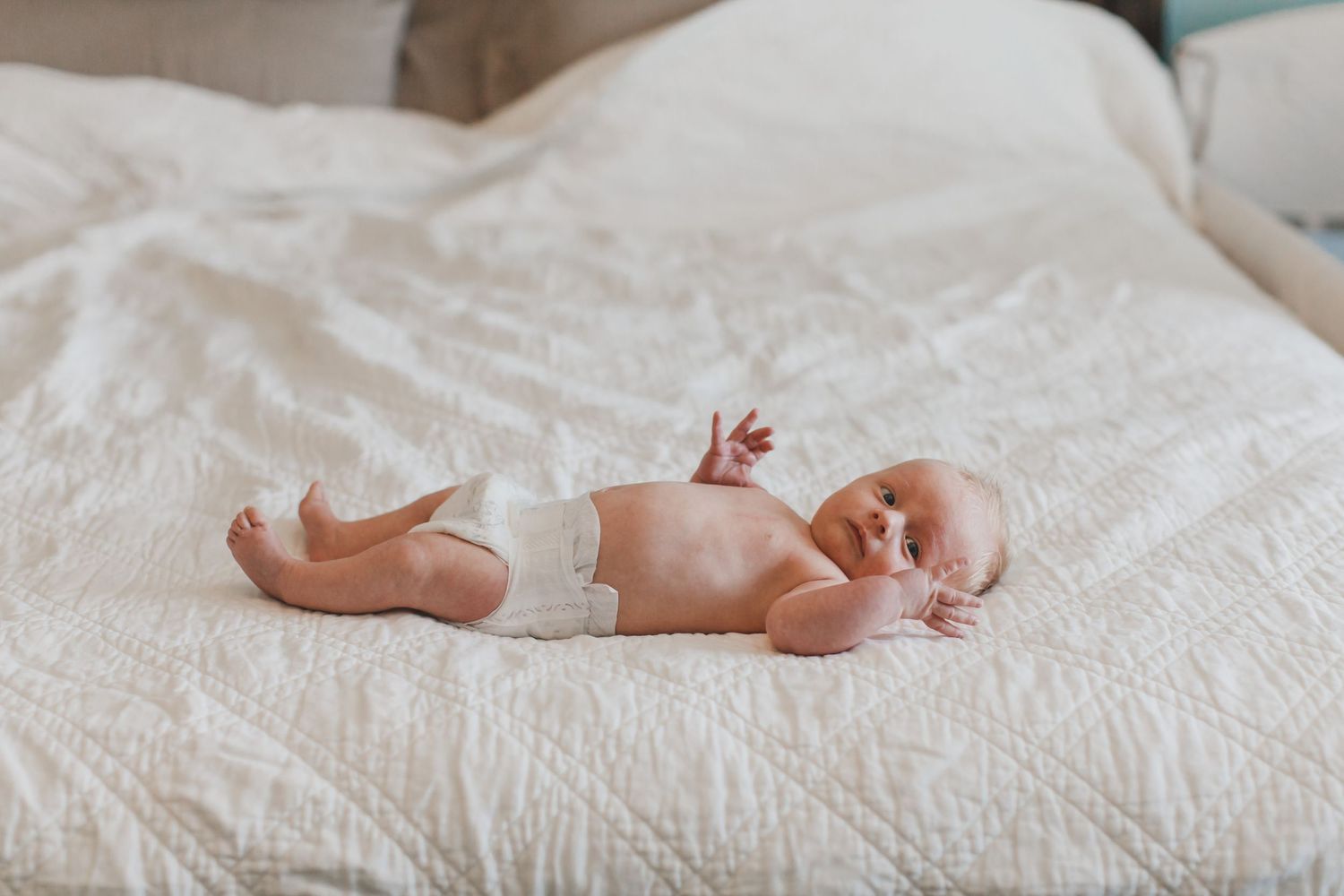 A sleeping newborn baby rests peacefully on white textured bedding.