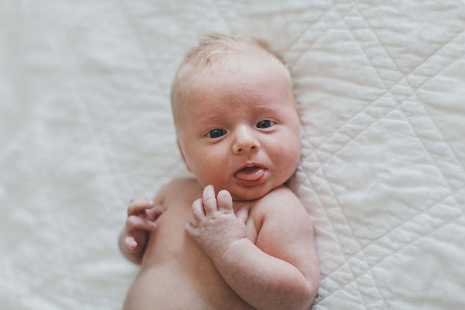 A newborn baby lies on white bedding showing various expressions and movements.