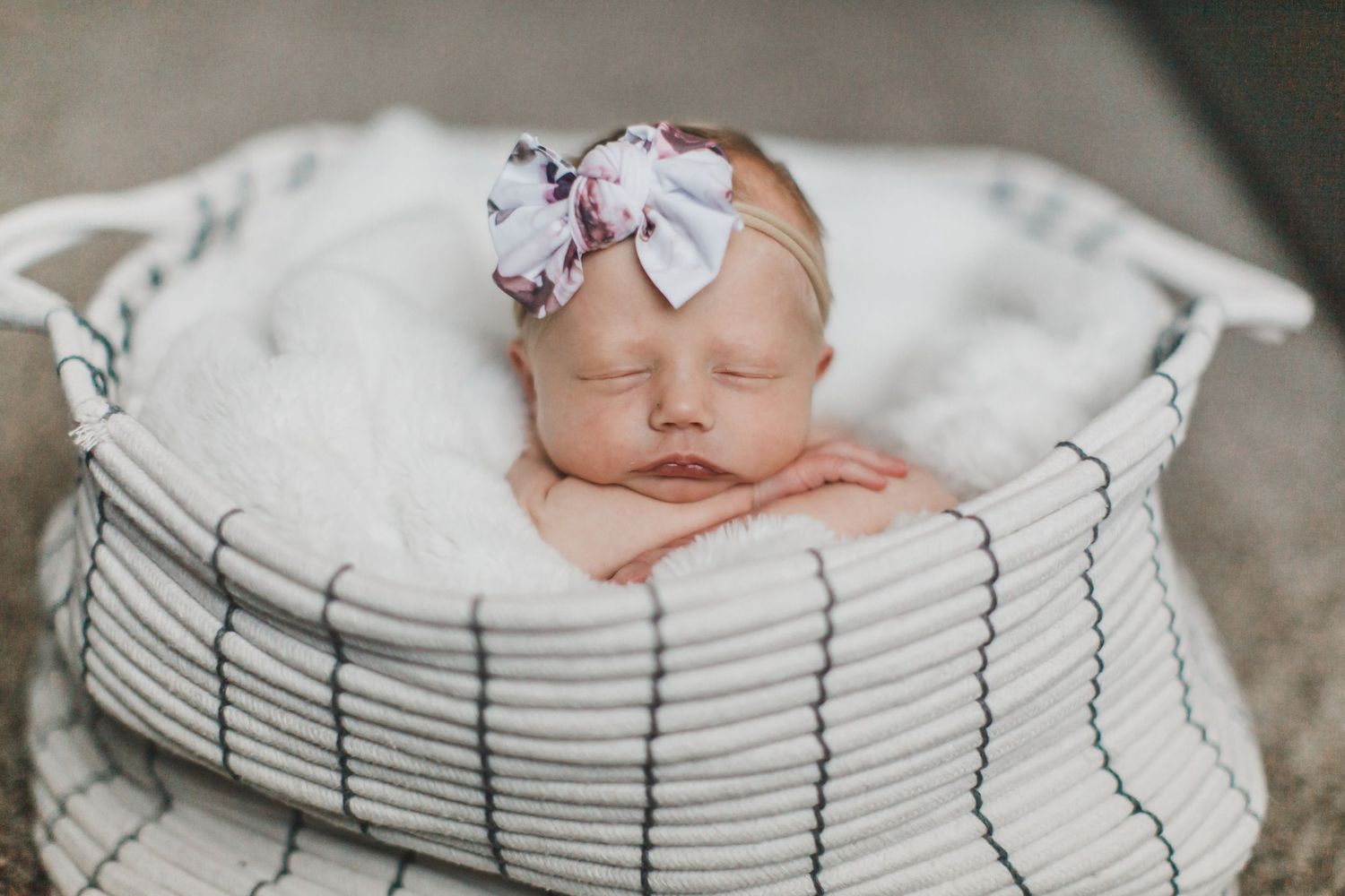 Sleeping newborn baby wearing a floral headband nestled in a striped blanket basket.