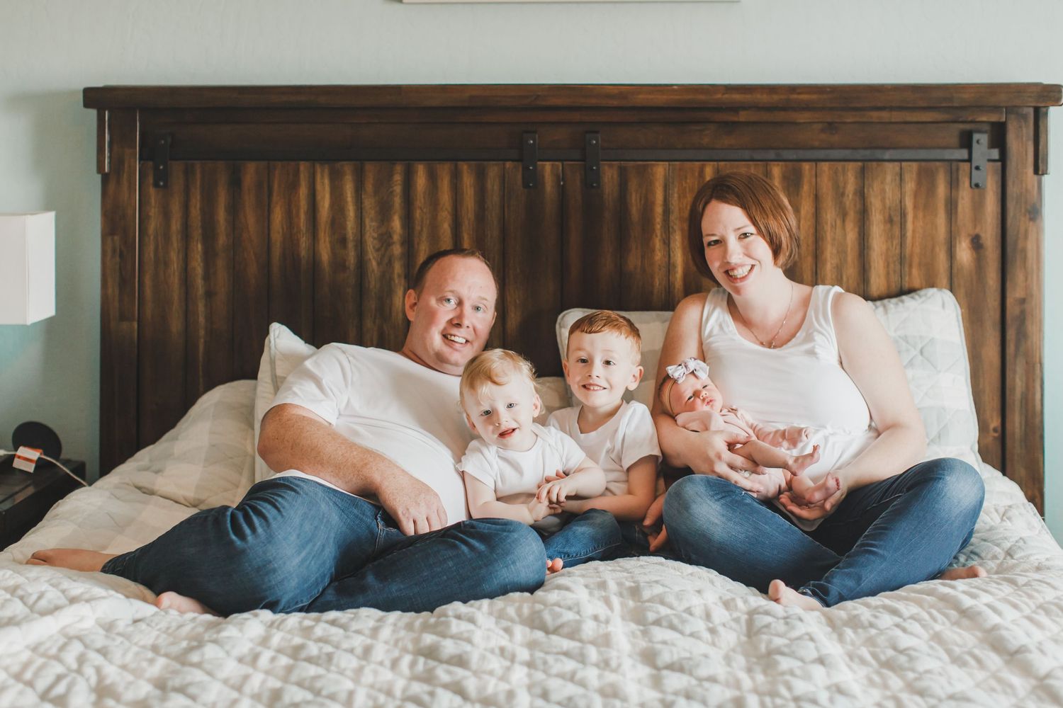 Family lounging together on bed with wooden headboard in casual lifestyle photoshoot.