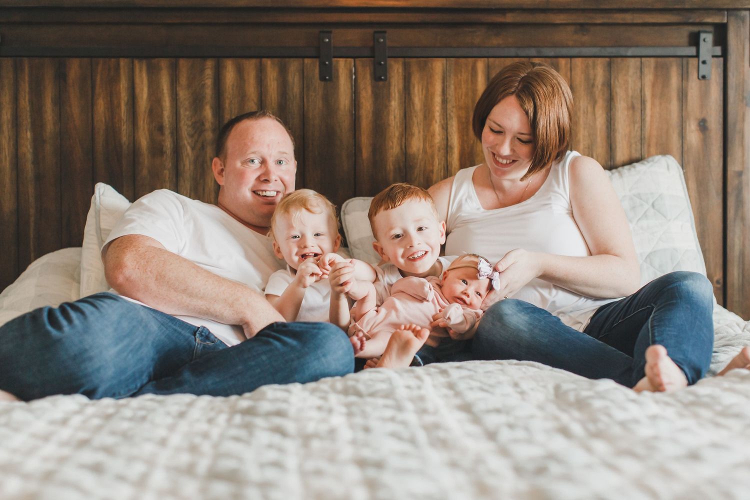 Candid family moments captured on bed with rustic wooden headboard.