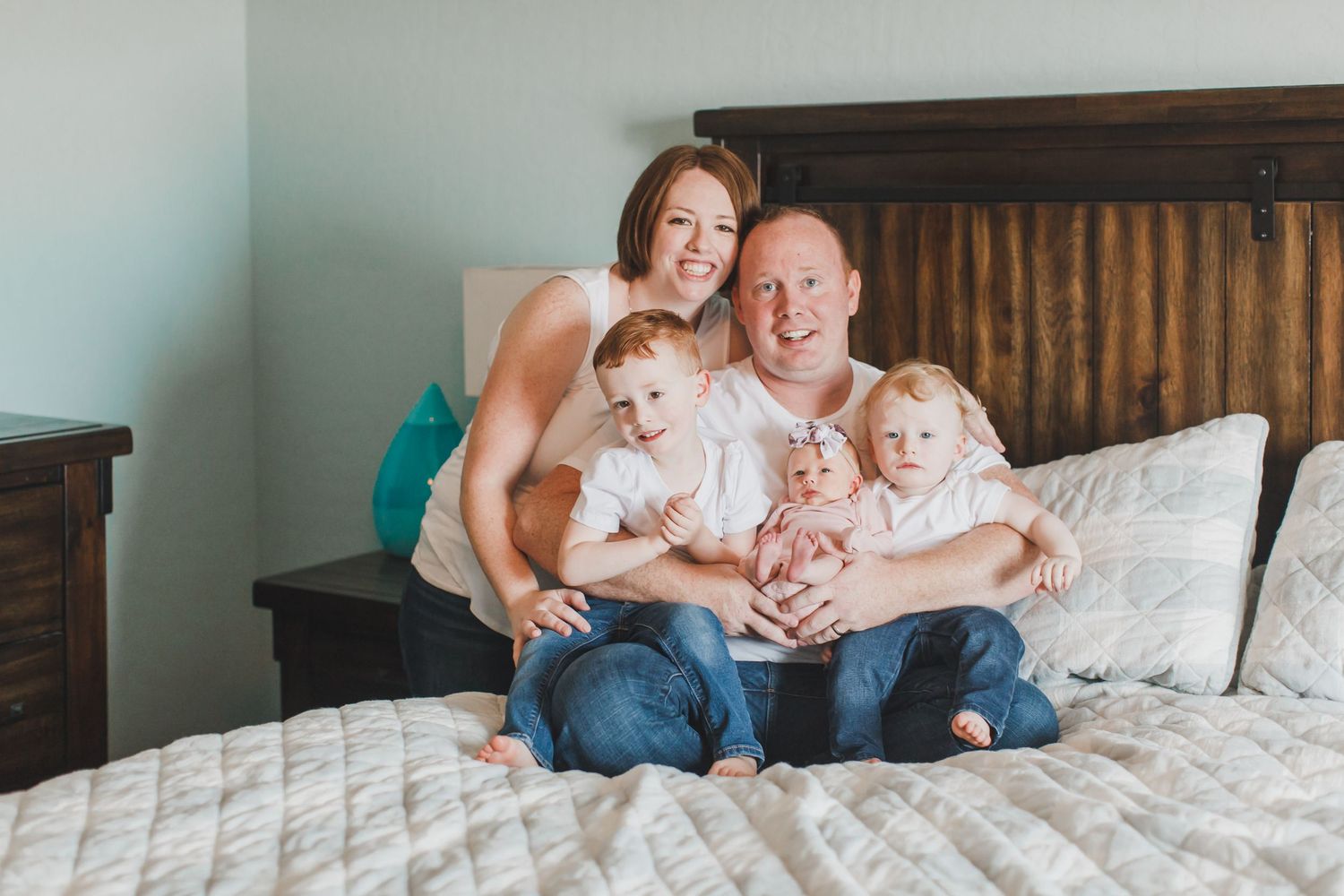Relaxed family portrait session on bed against wooden headboard and mint walls.