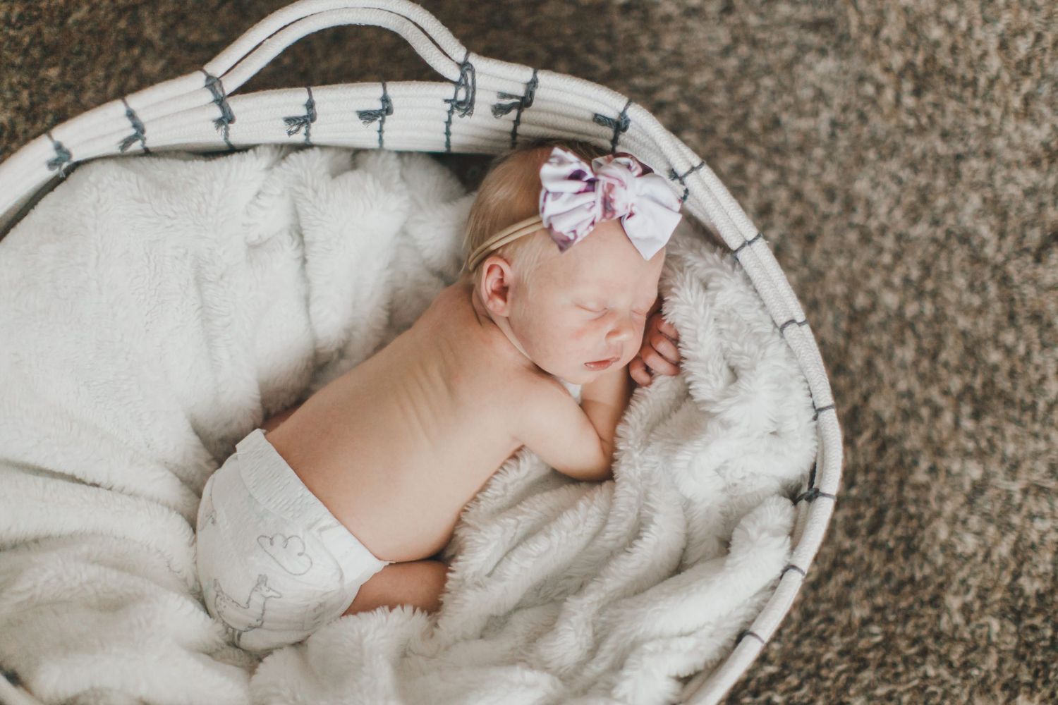 Peaceful newborn baby sleeping in white cushioned basket.