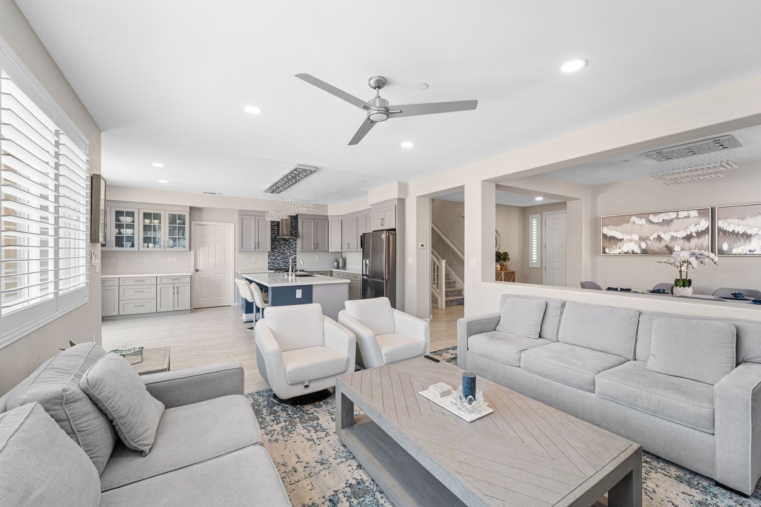 Modern coastal living room features white sofas, blue accents, and natural light streaming through large windows.