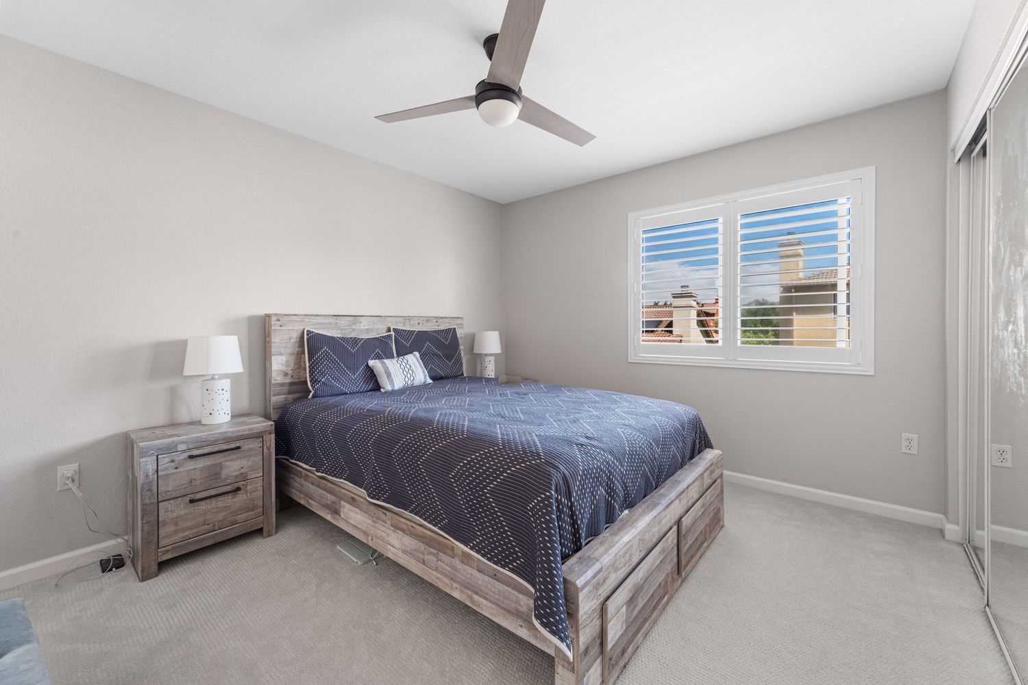 Modern bedroom interior with gray walls, ceiling fan, and blue bedding on a contemporary bed frame.
