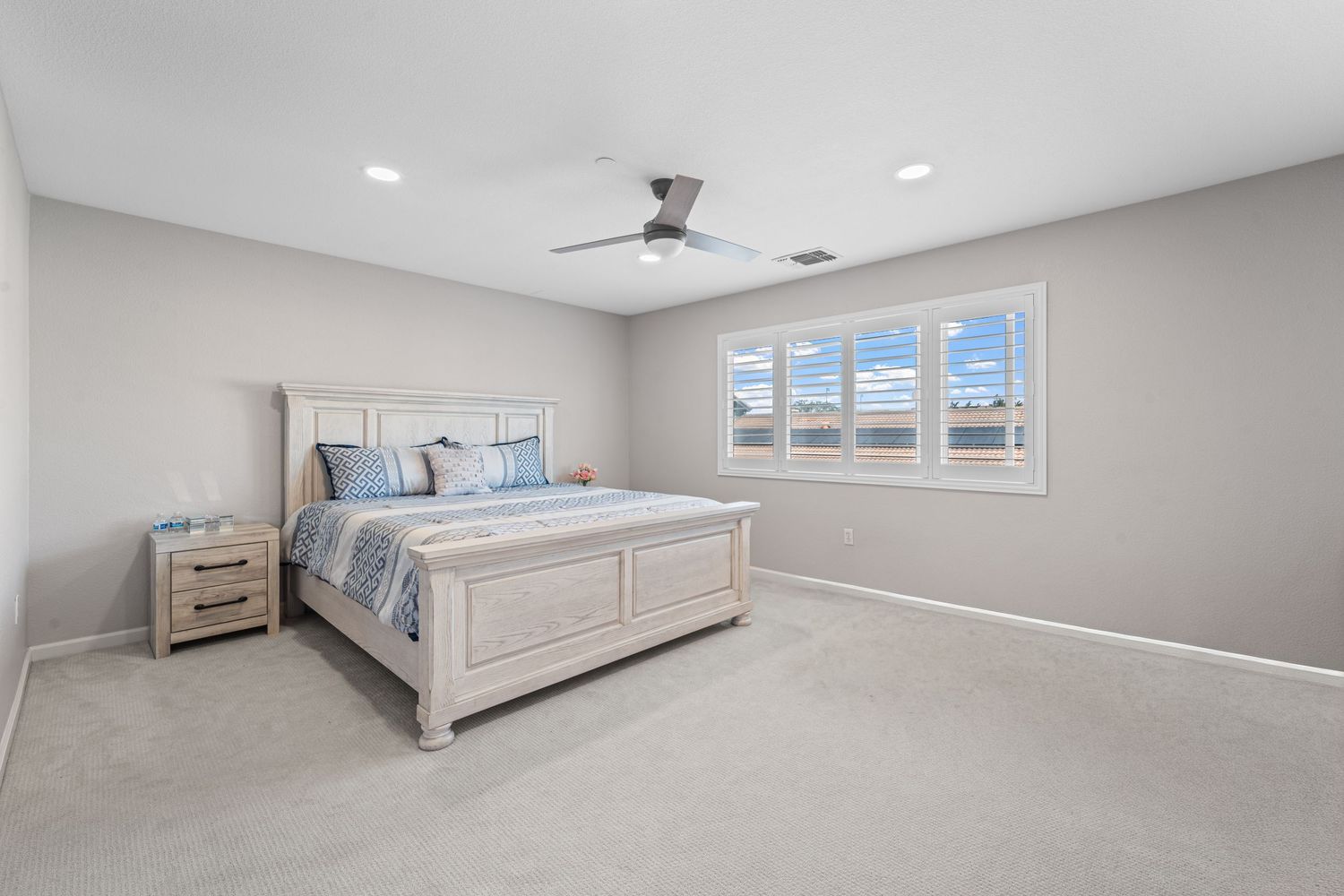 Spacious bedroom interior with large windows, neutral decor and plush carpeting.