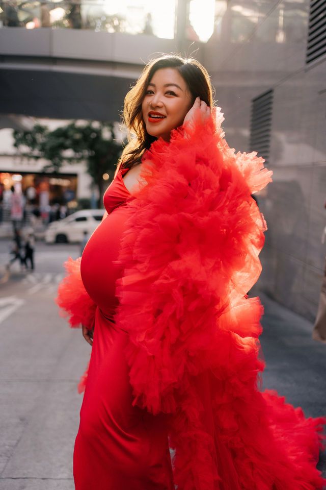 A person in a vibrant red dress with dramatic ruffled tulle details poses on an urban street at sunset.