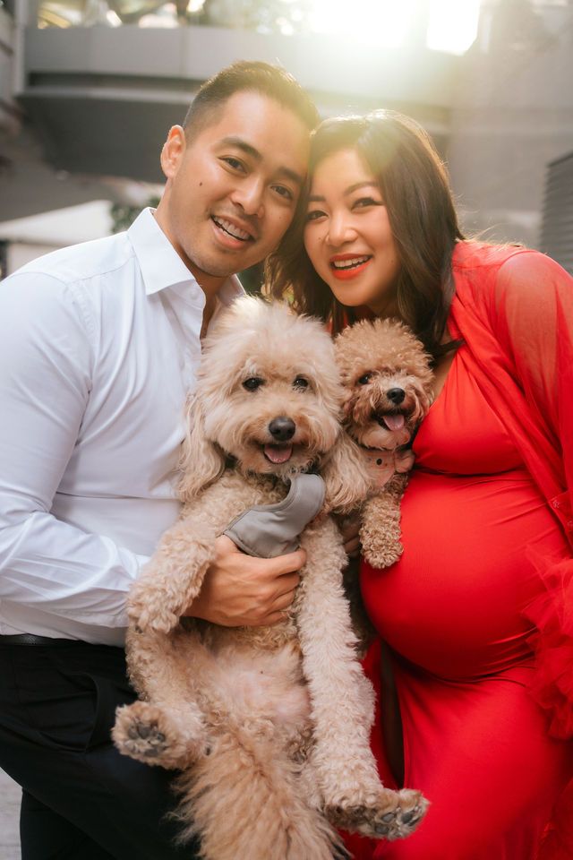 A couple in white and red outfits poses with their two fluffy cream-colored dogs for a series of loving portraits.
