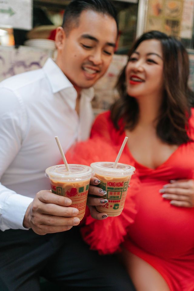 A couple in white and red outfits share iced coffee drinks and laughter during a casual cafe date.