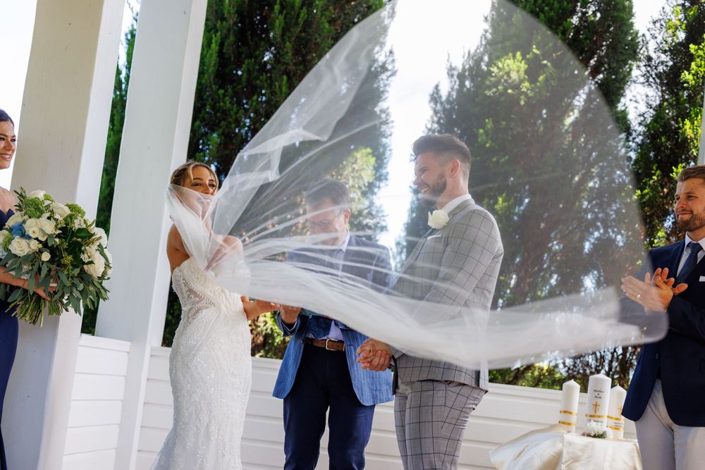 Bride's veil dramatically billowing in the wind during outdoor wedding ceremony.