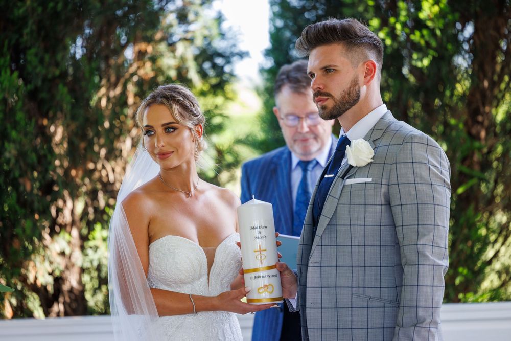 Bride and groom holding unity candle together during outdoor wedding ceremony.