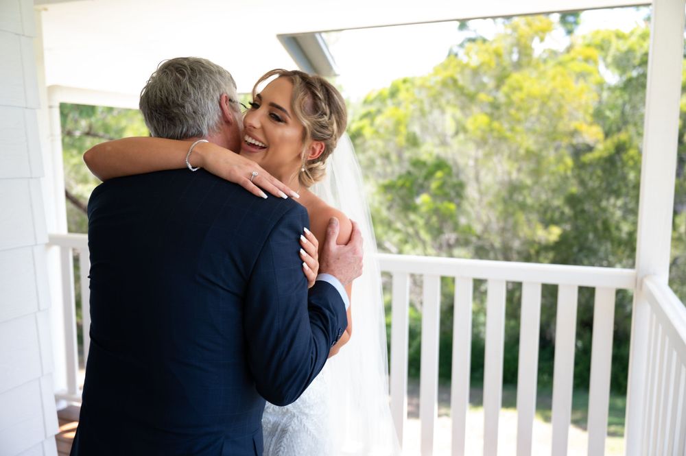 Bride shares emotional hug with father on porch before wedding ceremony.