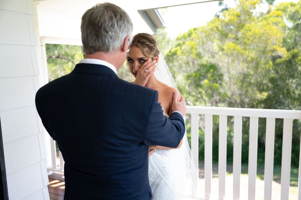 Father tenderly holds brides face during emotional first look moment on porch.
