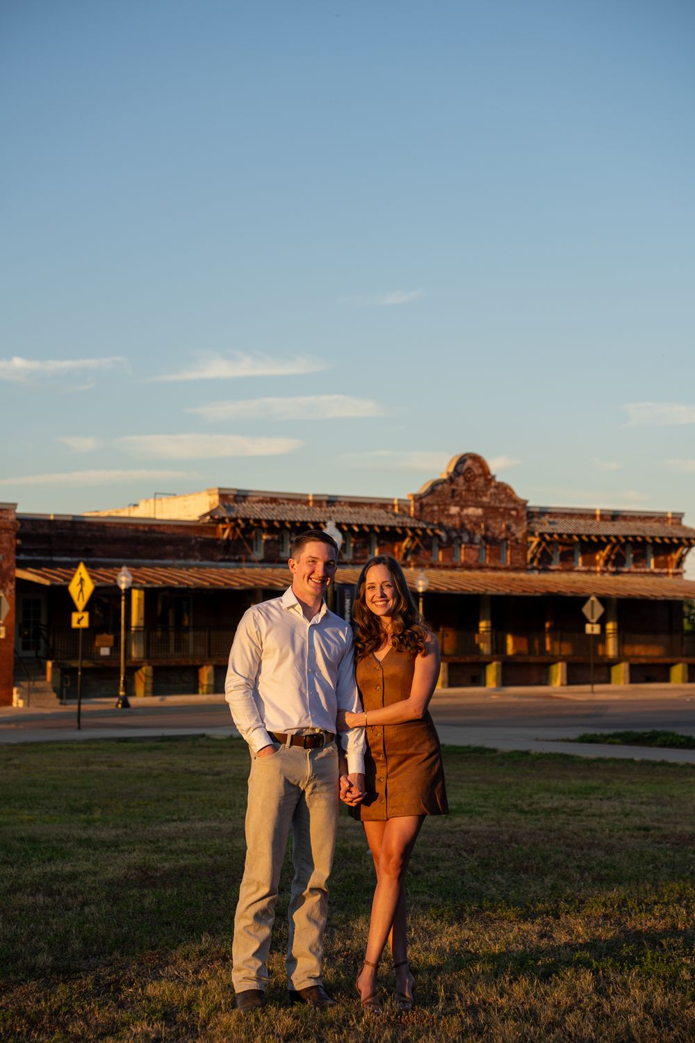 A couple stands together at sunset in front of rustic wooden buildings at a rural venue.