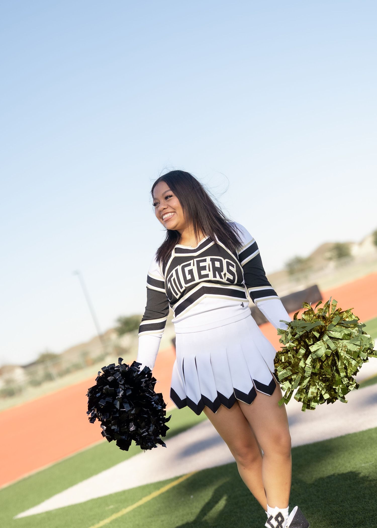 Teen cheerleader standing on turf in navy and gold uniform holding pom-poms