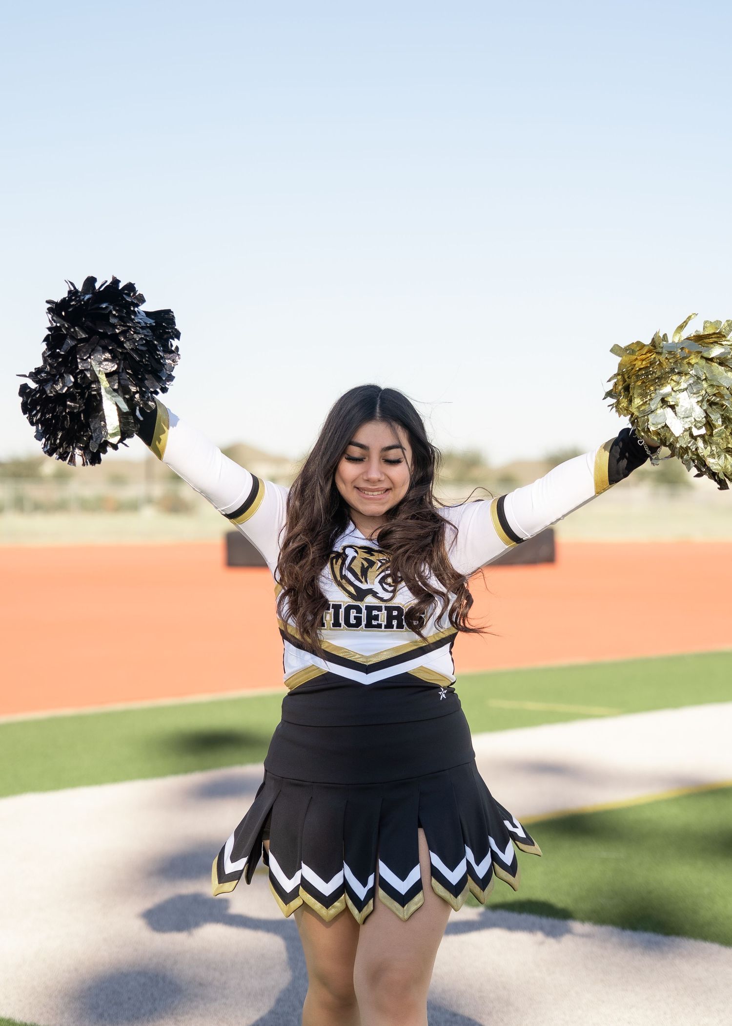 Teen cheerleader standing on turf in navy and gold uniform holding pom-poms