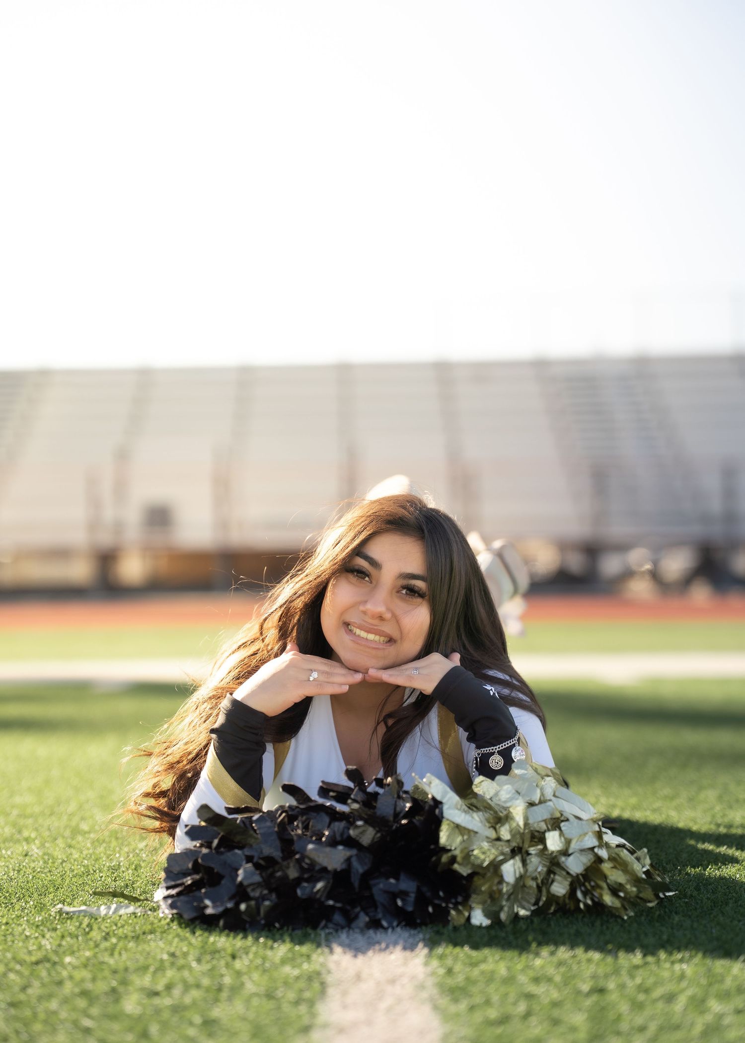 Teen cheerleader standing on turf in navy and gold uniform holding pom-poms