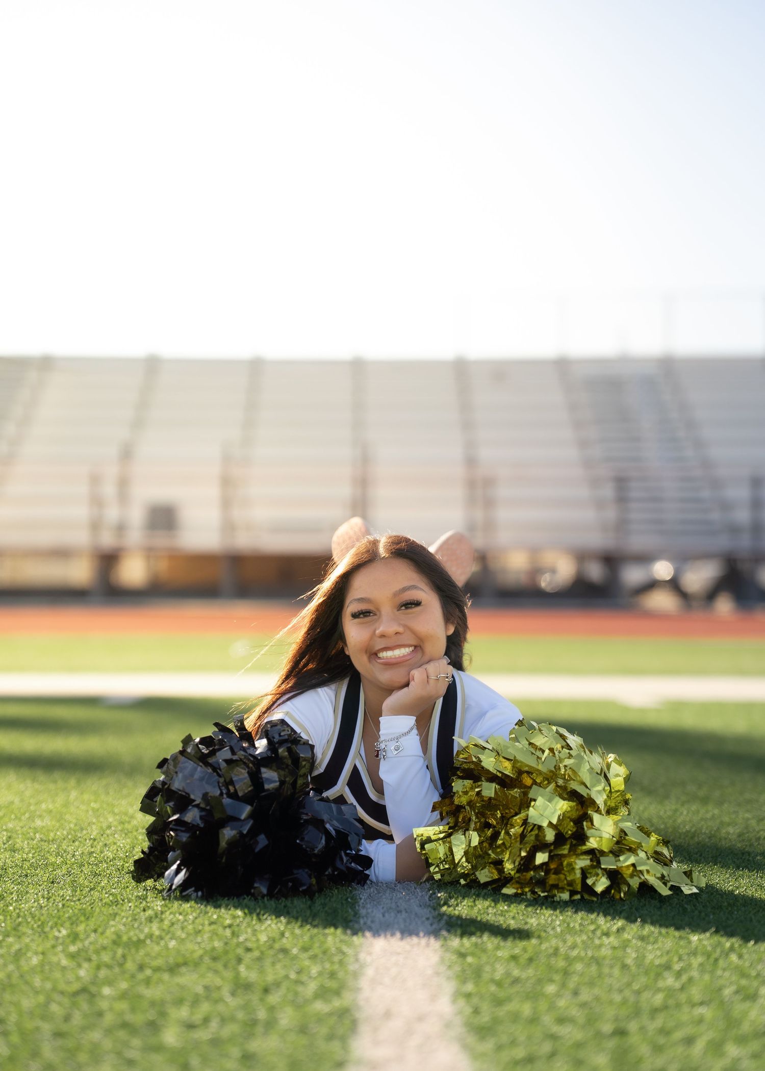 Teen cheerleader standing on turf in navy and gold uniform holding pom-poms