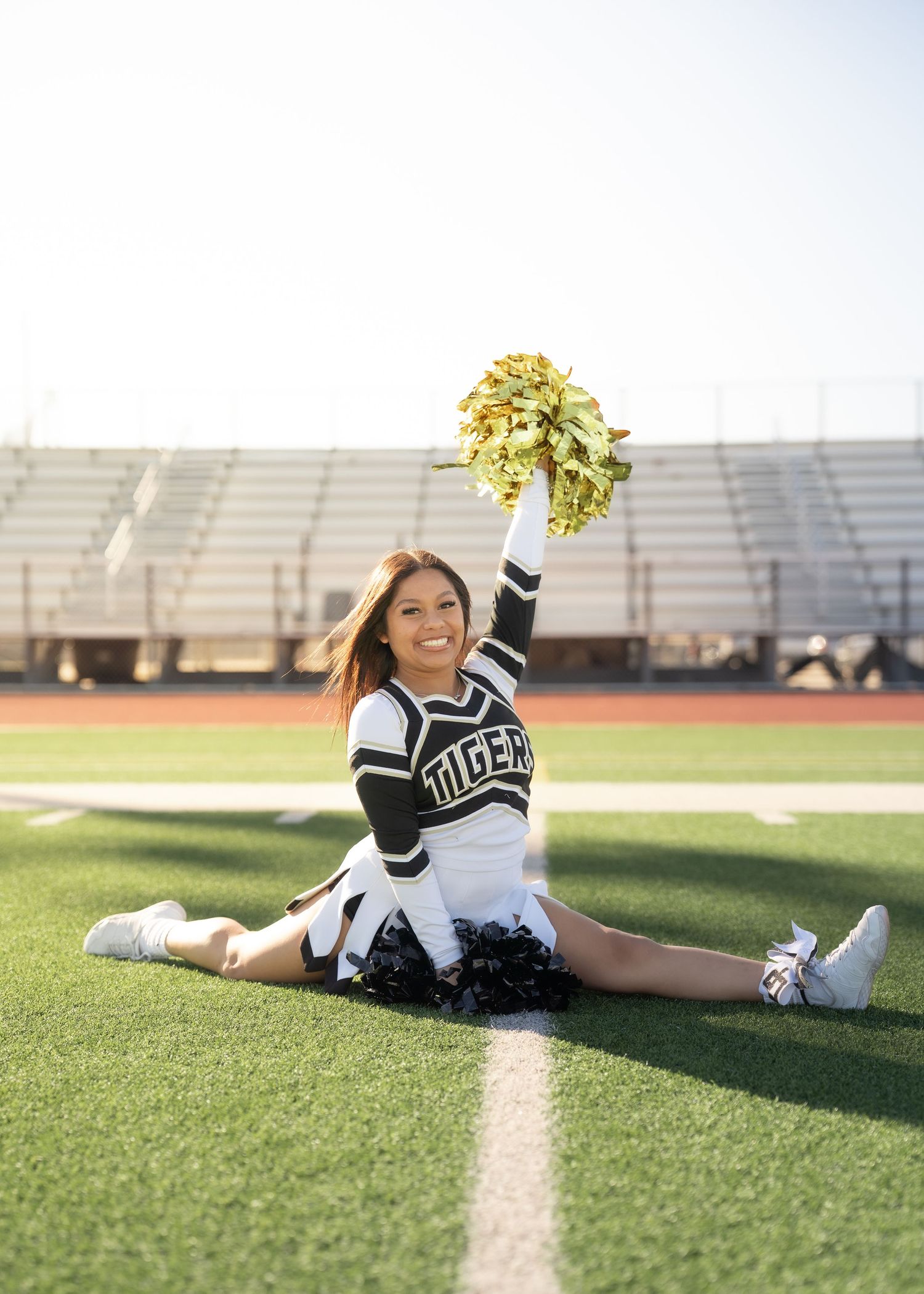 Teen cheerleader standing on turf in navy and gold uniform holding pom-poms