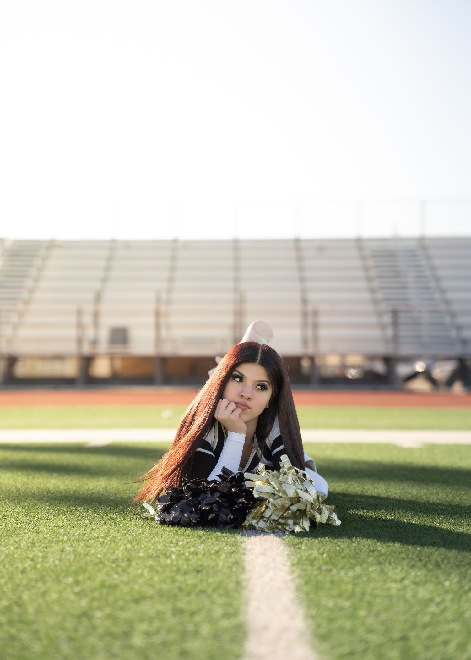 Teen cheerleader standing on turf in navy and gold uniform holding pom-poms