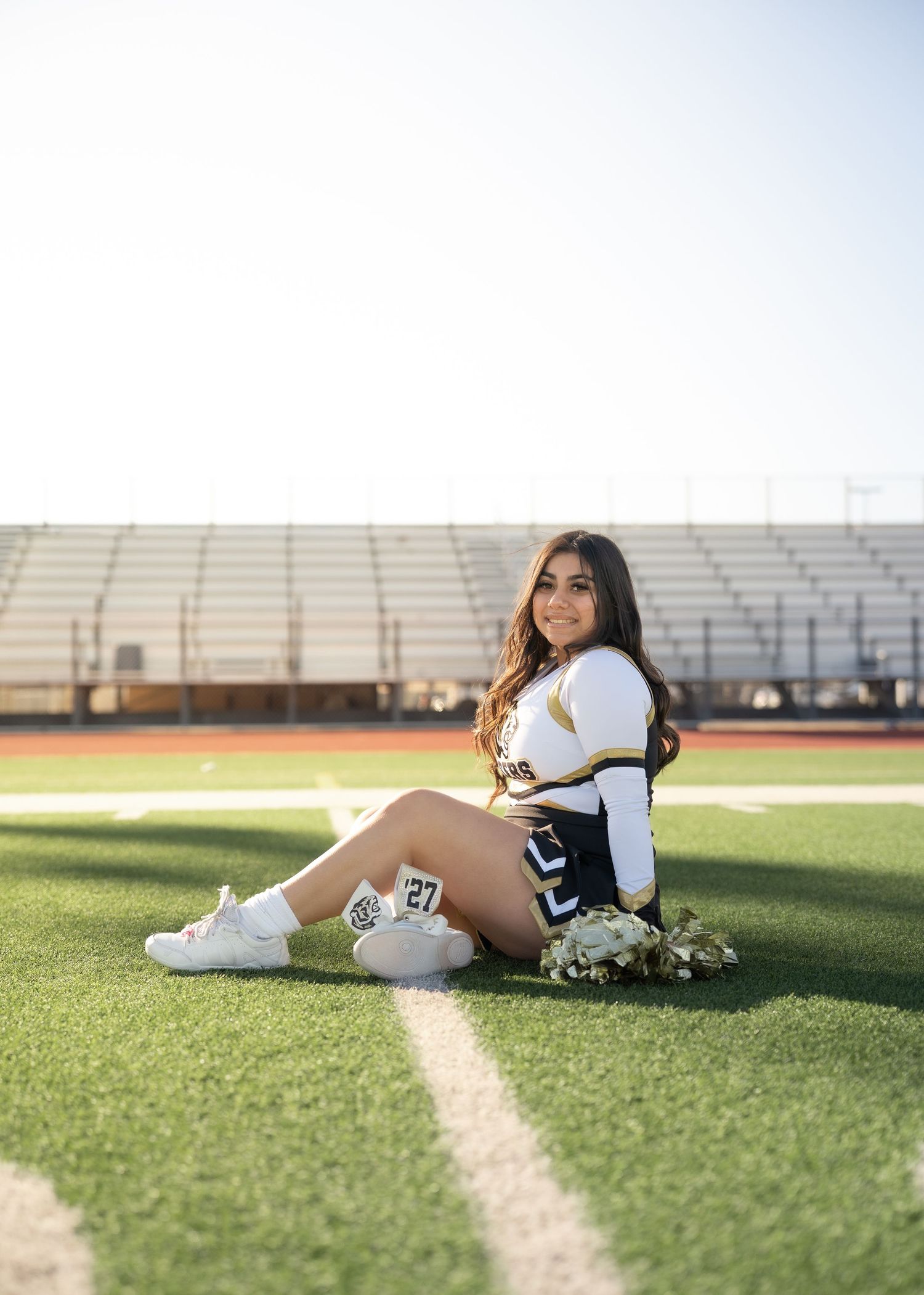Teen cheerleader standing on turf in navy and gold uniform holding pom-poms