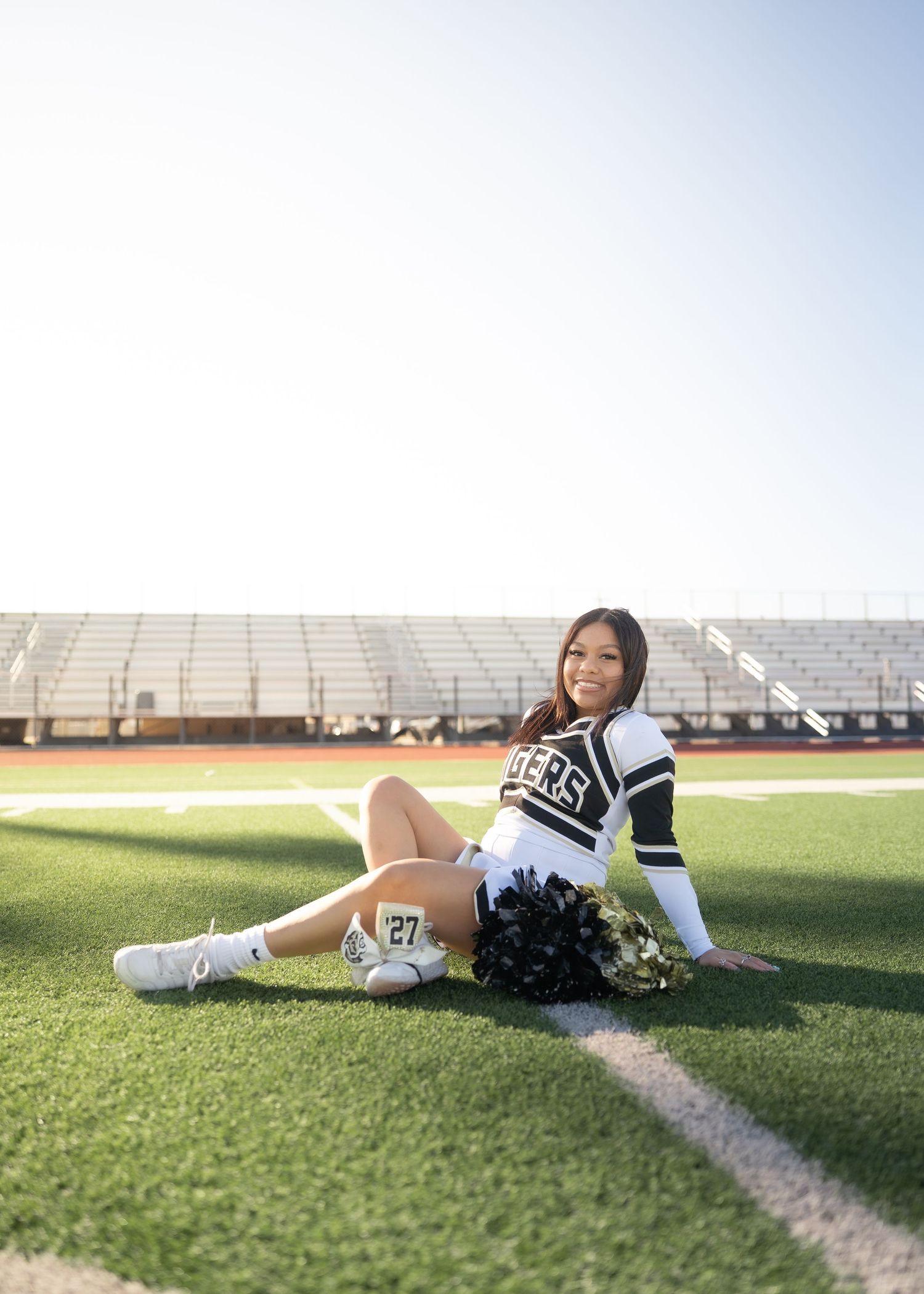 CyPark High cheerleader posing on football field with pom-poms, smiling in uniform